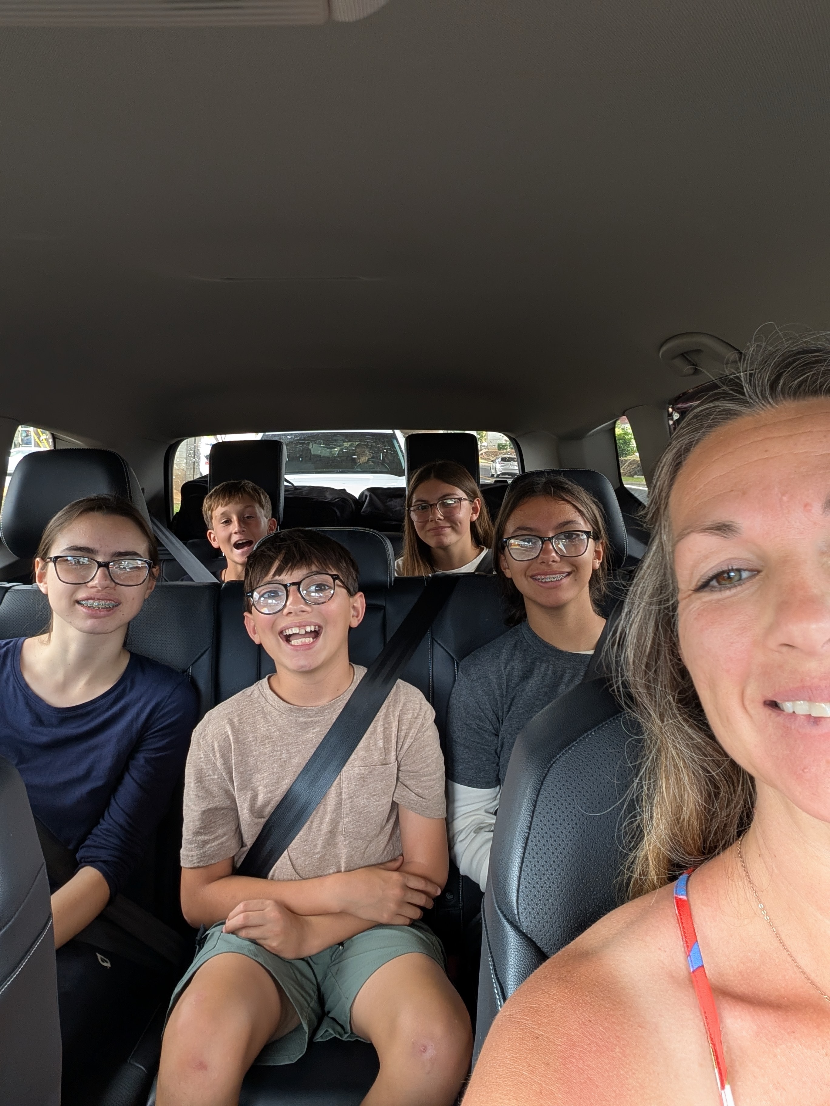 Mom and five kids smiling in the car ready for a road trip